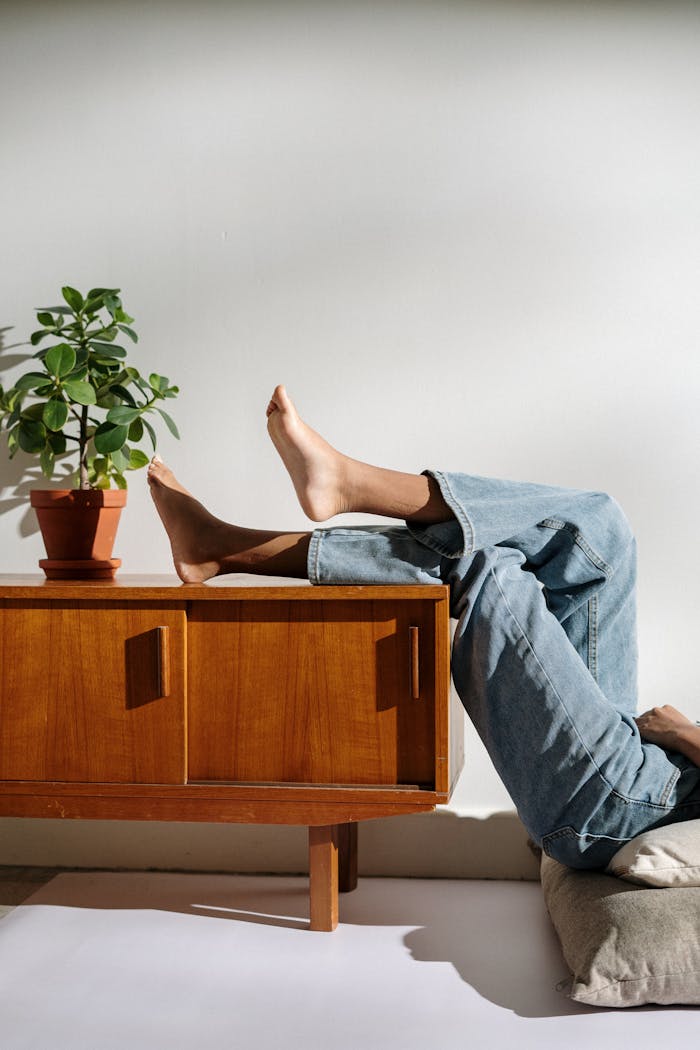 Person in Blue Denim Jeans Lying on Brown Wooden Table